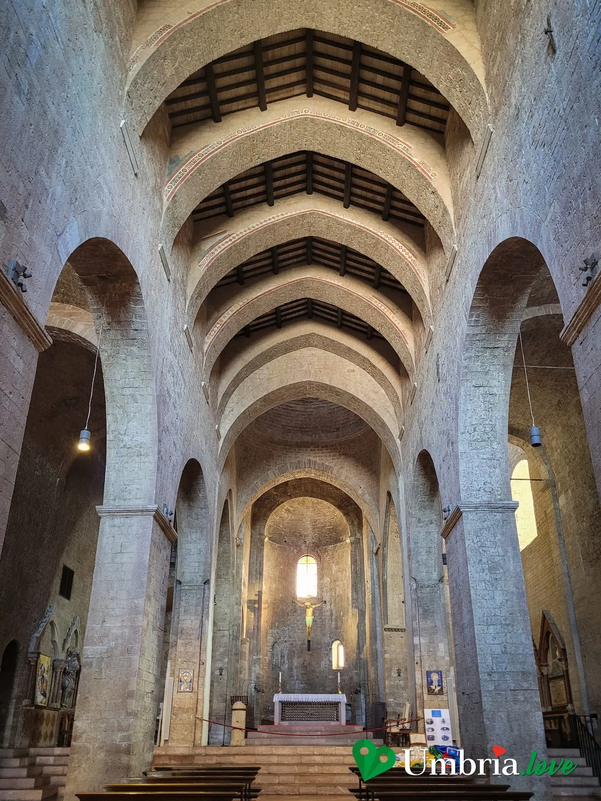 L'interno a tre navate dell'abbazia di San Pietro ad Assisi, con il soffitto a capriate e le pareti nude in pietra