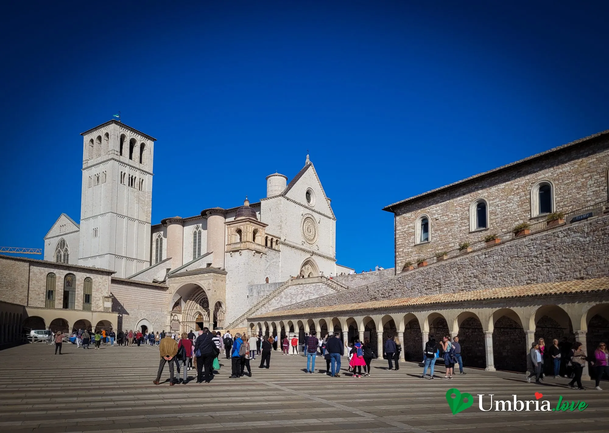 Il loggiato rinascimentale sulla piazza inferiore della Basilica di San Francesco ad Assisi, con le arcate e la gente che passeggia