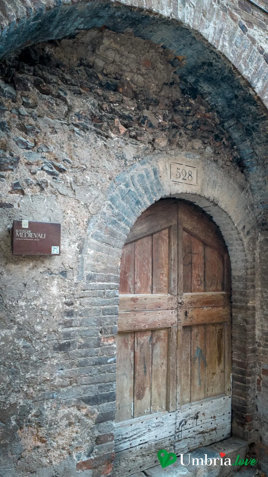 Il grande arco a tutto sesto di una bottega medievale di Trevi, con il portone di legno