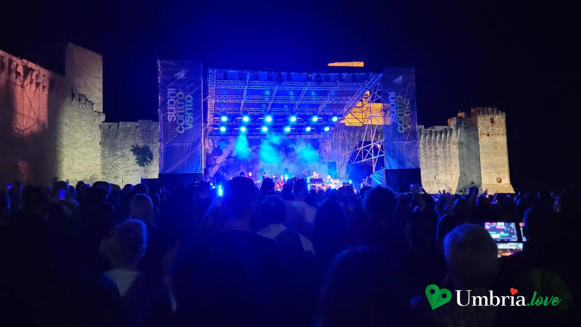 Un concerto serale davanti alla Rocca Maggiore di Assisi, con il palco illuminato e la fortezza sullo sfondo