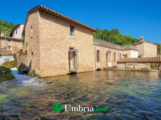 Le case di pietra di Rasiglia sull'acqua limpida di un canale, con un ponticello e la montagna boscosa alle spalle