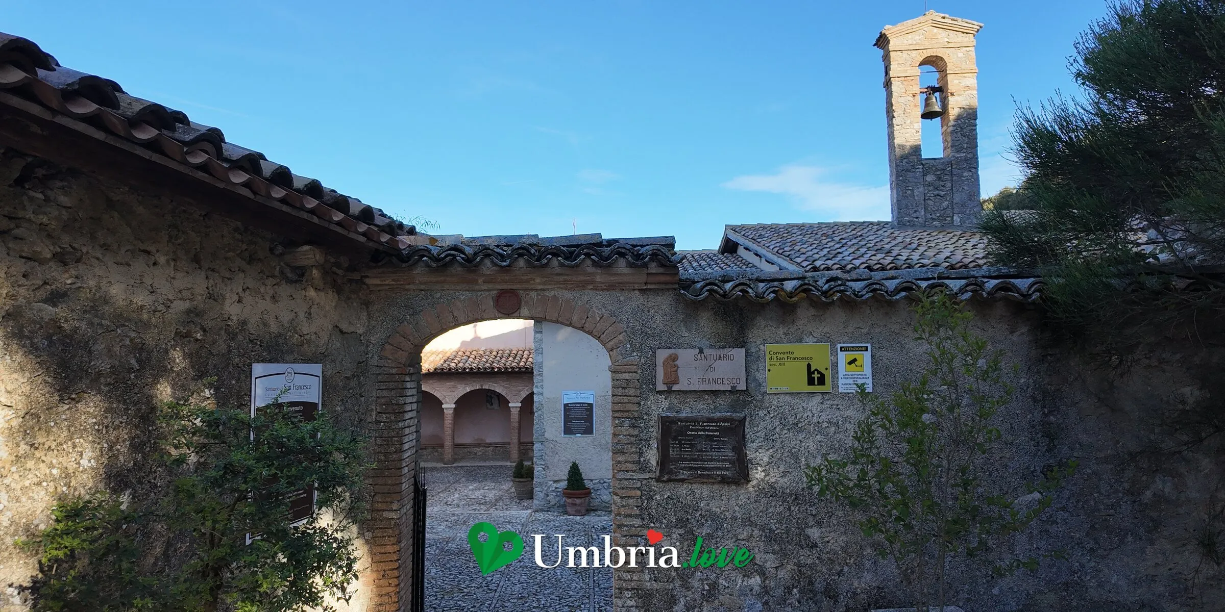L'ingresso del Santuario di San Francesco al Monteluco, sopra Spoleto: l'arco nel muro di pietra e il campanile a vela sul convento
