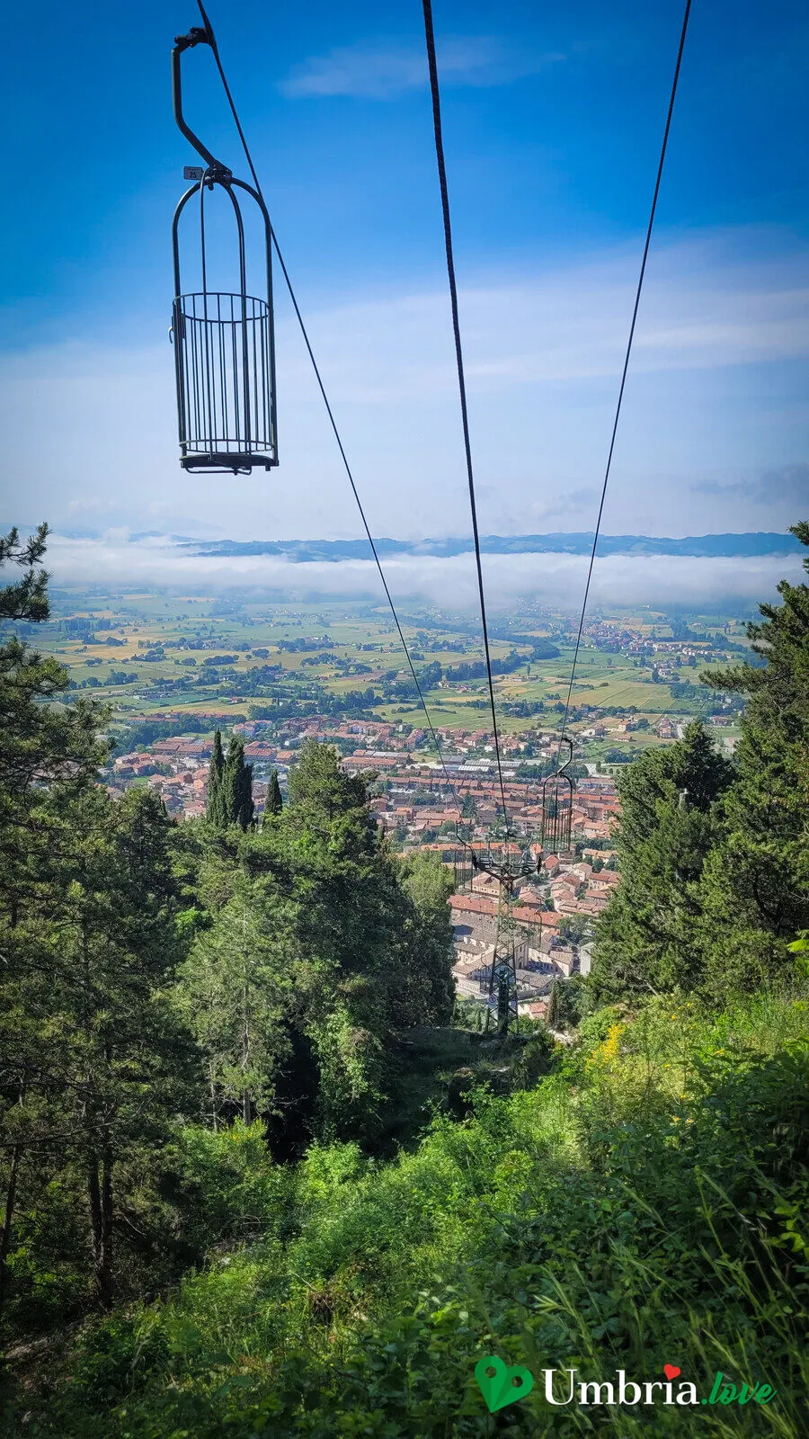 Una cabina aperta della funivia Colle Eletto di Gubbio sul cavo, con la pianura eugubina sullo sfondo