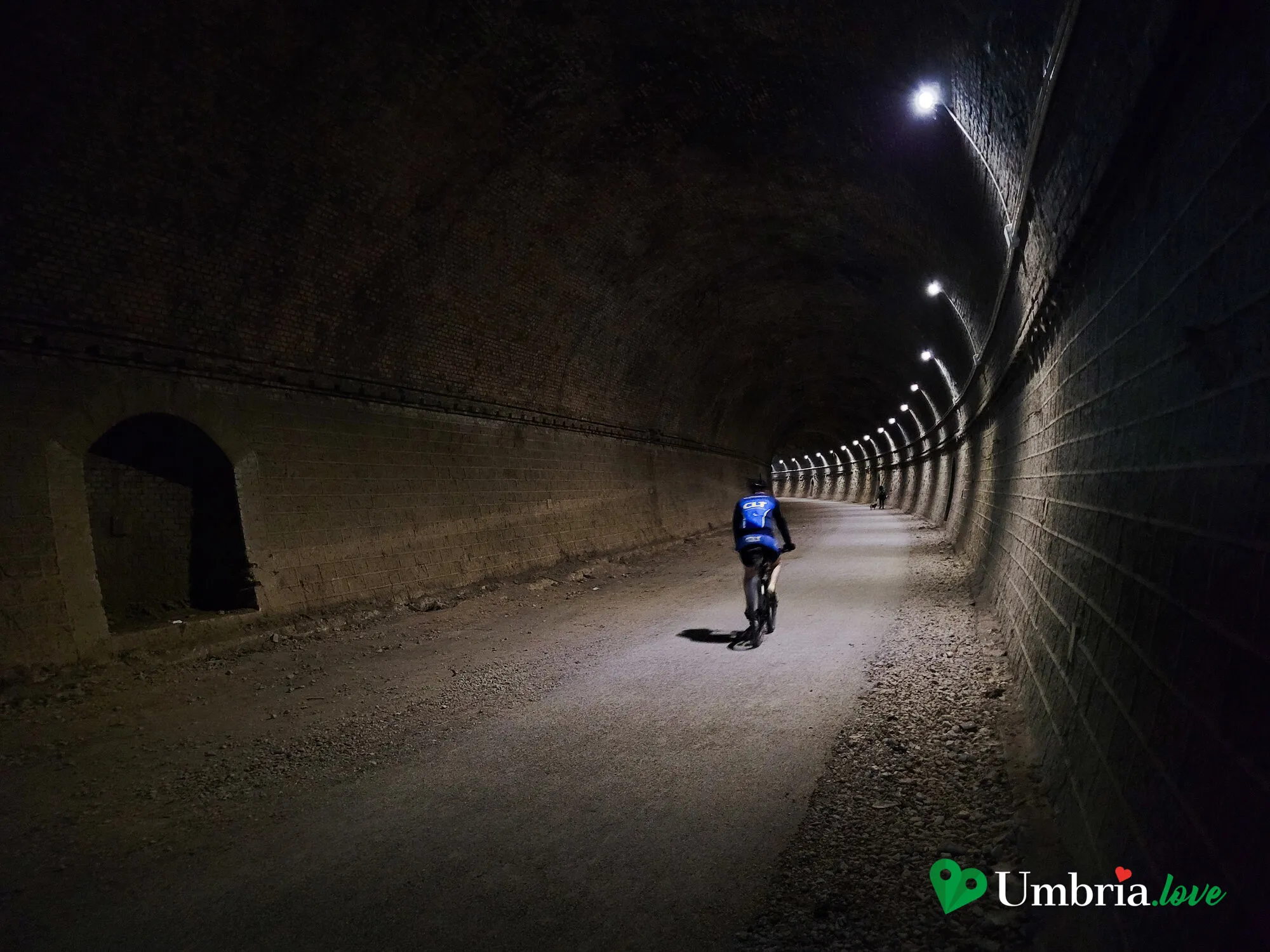 Una delle gallerie illuminate lungo il sentiero dell'ex ferrovia, con un ciclista in controluce