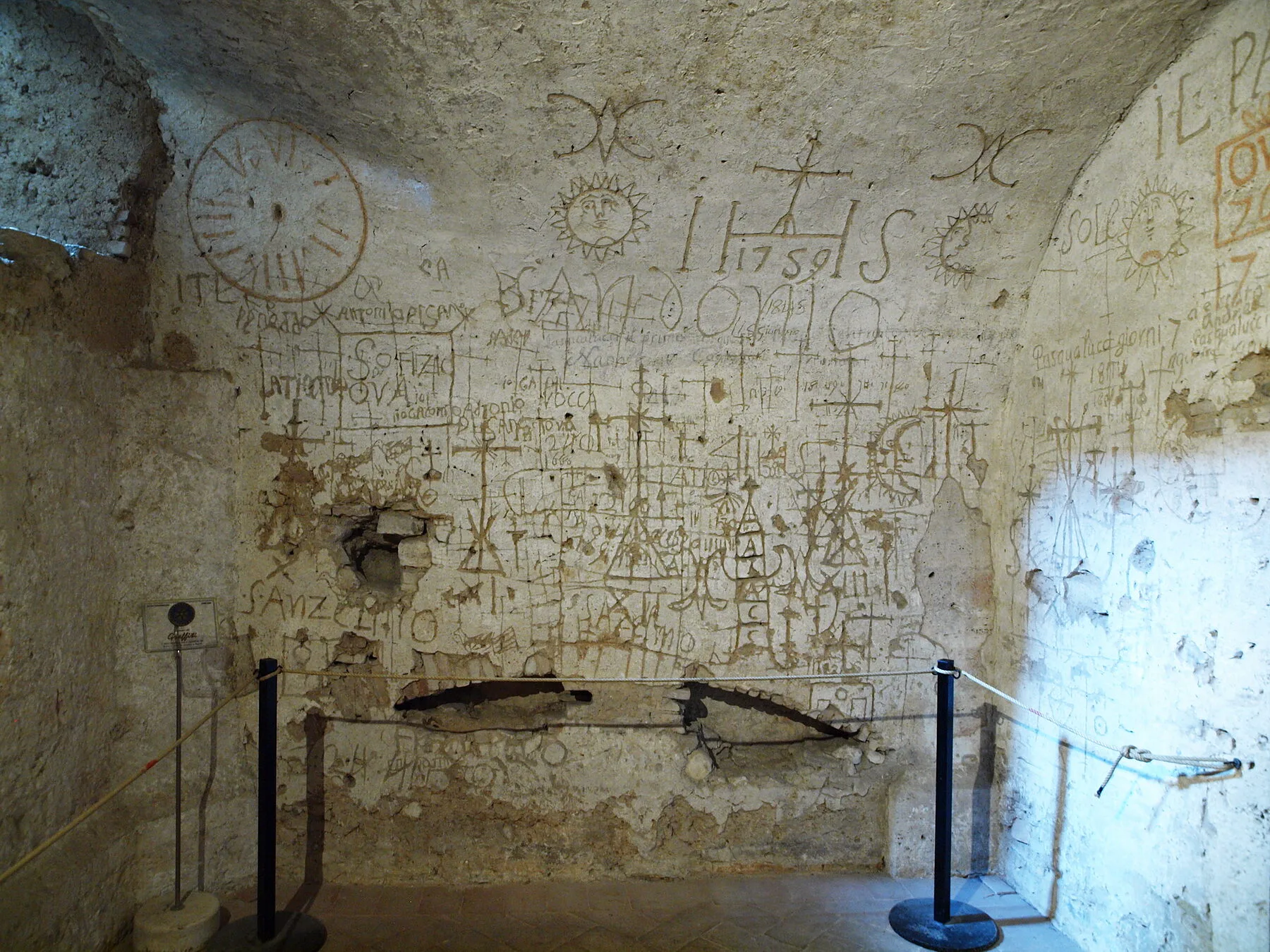 La parete della cella di Narni Sotterranea coperta dai graffiti del prigioniero Giuseppe Andrea Lombardini: soli, croci, simboli e la data 1759