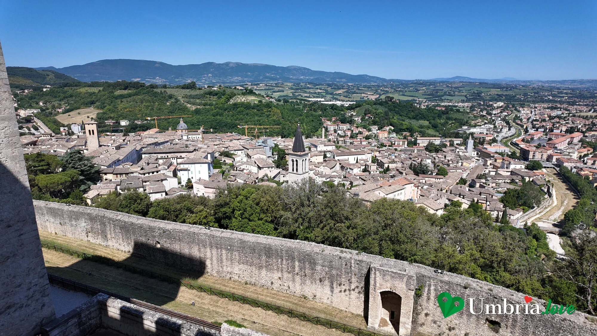 Spoleto vista dall'alto dai camminamenti della Rocca: i tetti del centro storico, i campanili e la Valle Umbra che si apre verso nord