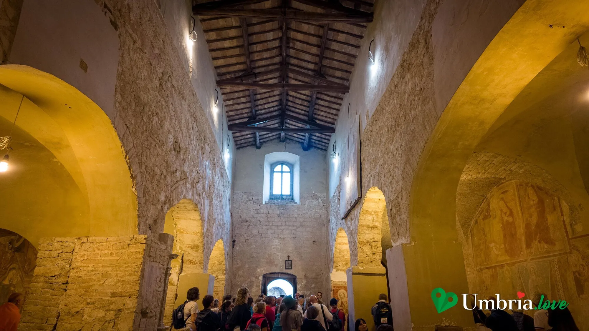 L'interno di Santa Maria di Pietrarossa a Trevi: pilastri in pietra, tetto a capriate e affreschi sulle pareti