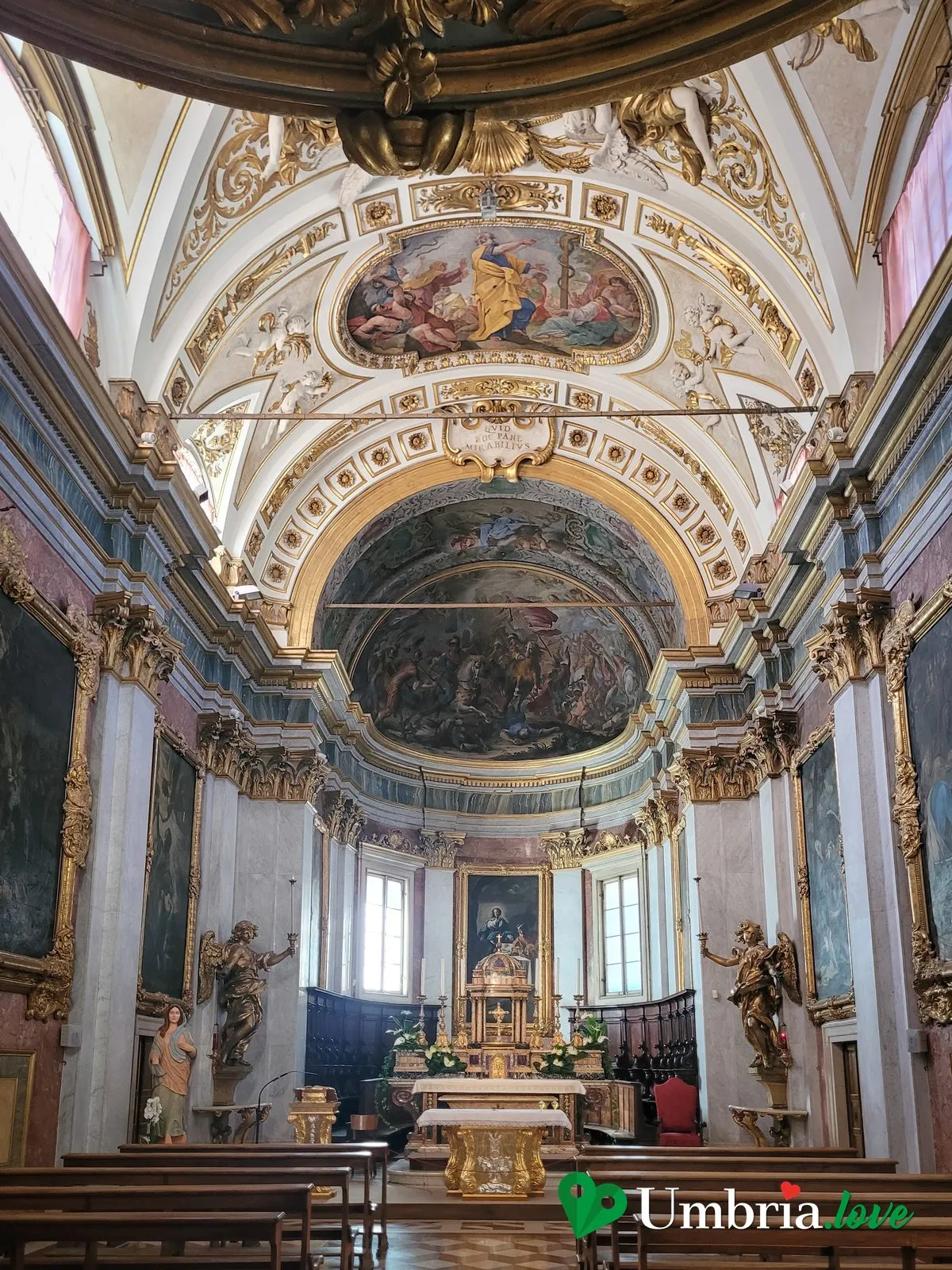 L'interno barocco della Cattedrale di San Rufino ad Assisi, con la volta affrescata, le statue di angeli e il coro ligneo dietro l'altare maggiore