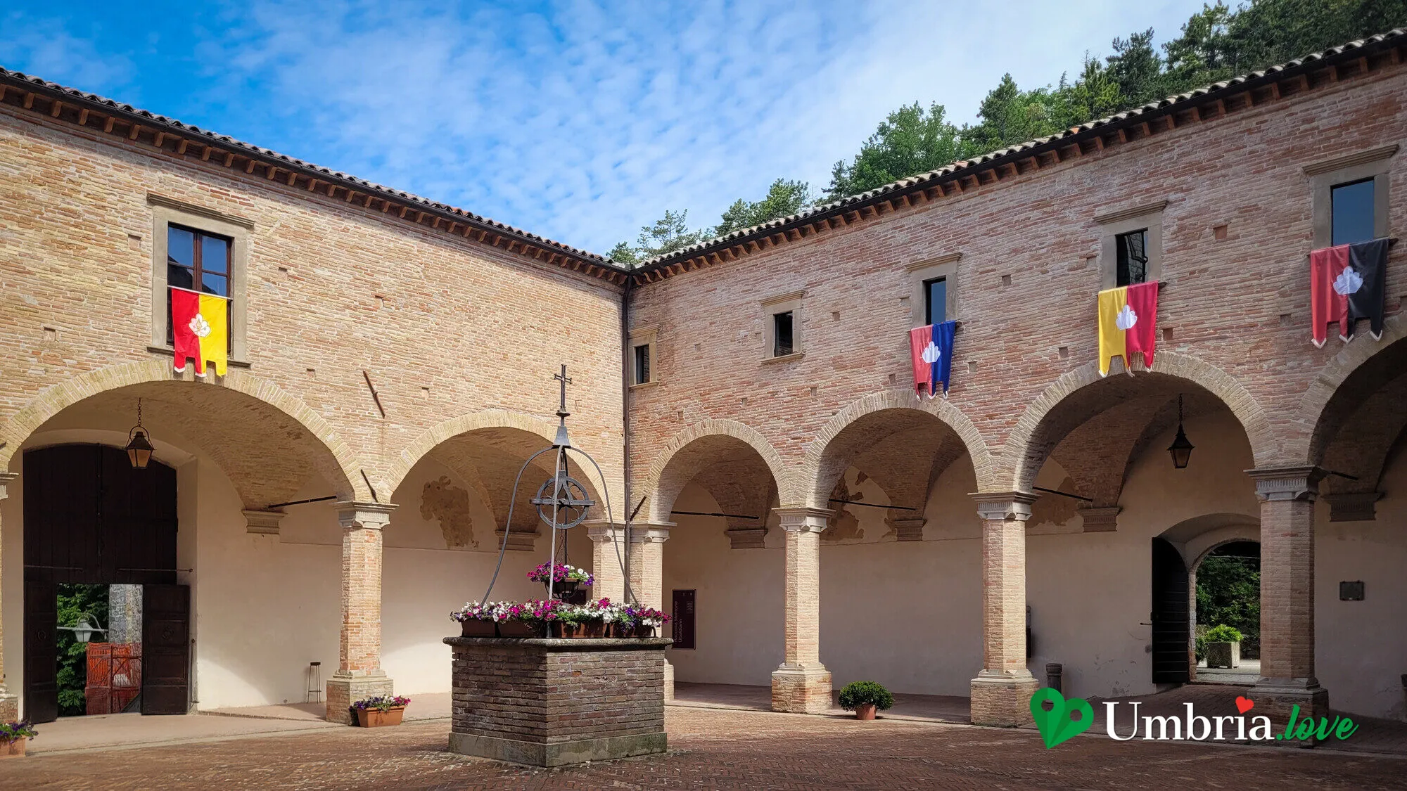 Il chiostro in mattoni della Basilica di Sant'Ubaldo a Gubbio, con il pozzo al centro e le bandiere dei quartieri