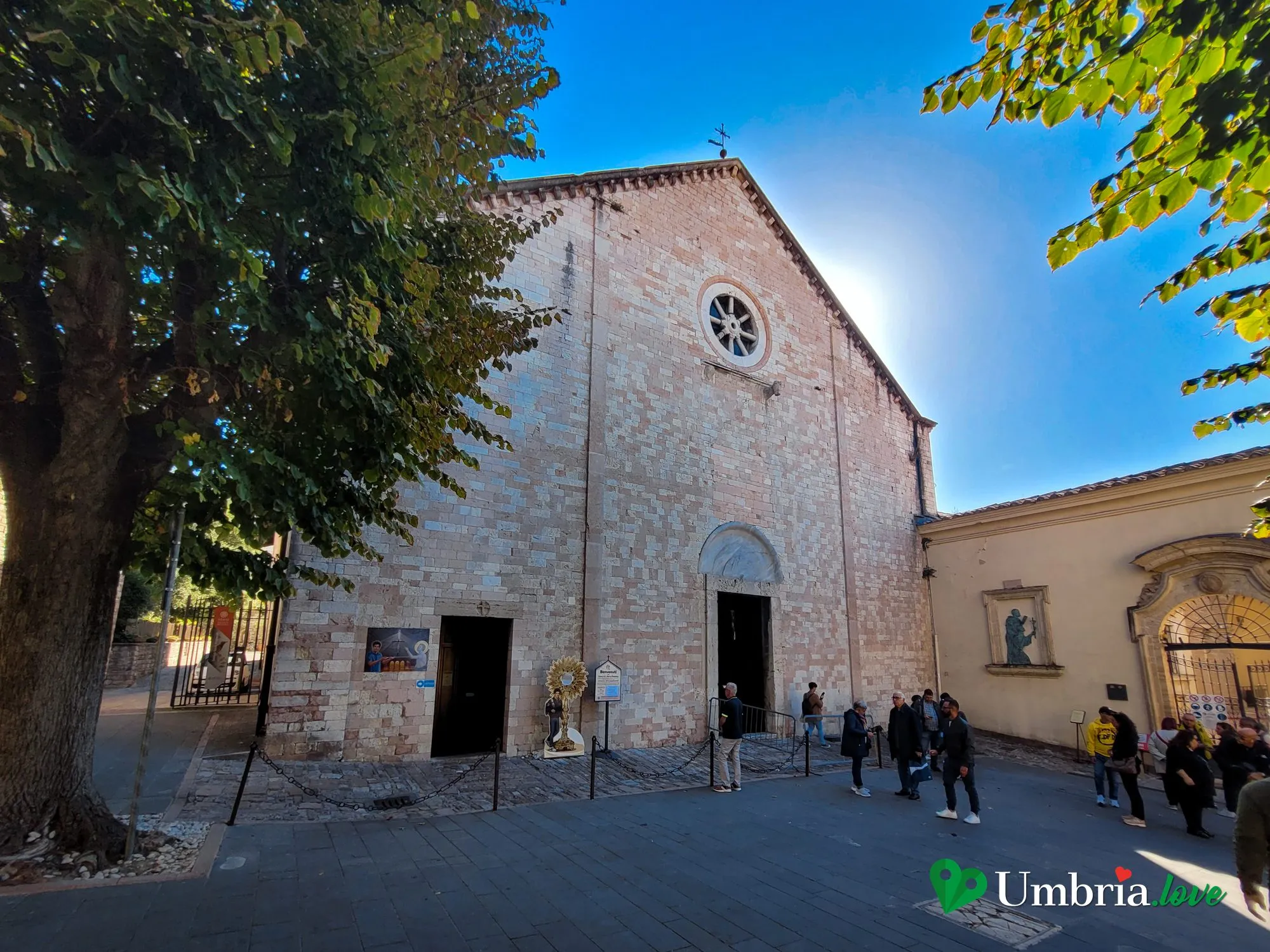 La facciata romanica della chiesa di Santa Maria Maggiore ad Assisi, il Santuario della Spogliazione, con il rosone, sulla piazza alberata del vescovado