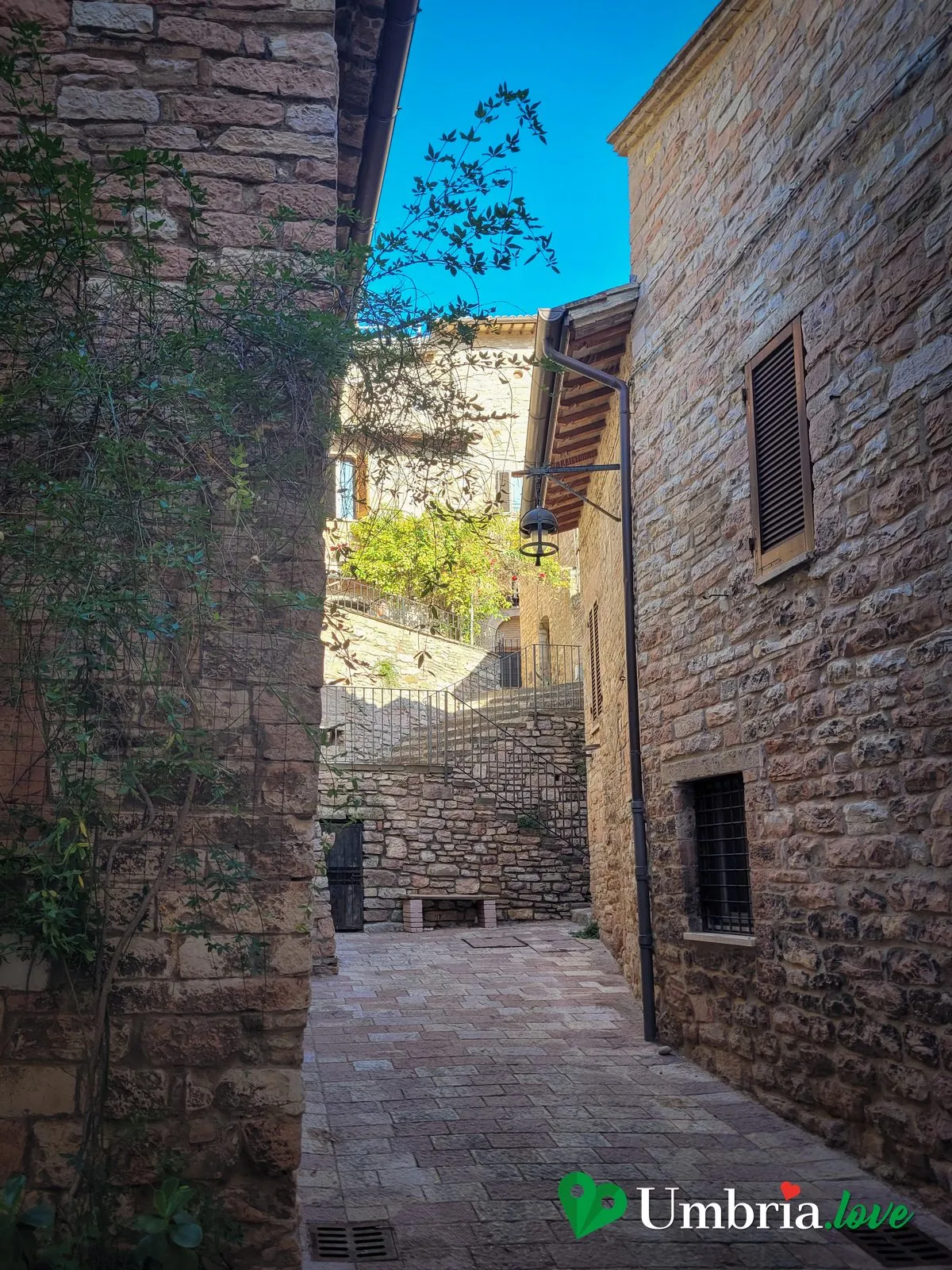 Un vicolo a gradoni di Assisi tra le case di pietra rosa, in salita verso la parte alta della città
